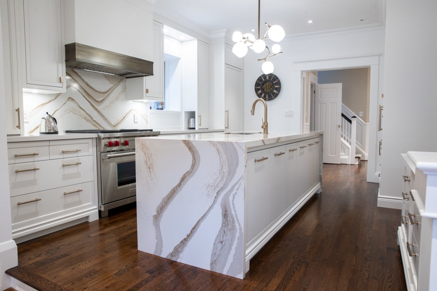 Custom-built kitchen with white cabinets, large island with waterfall marble countertop, and wood floors.